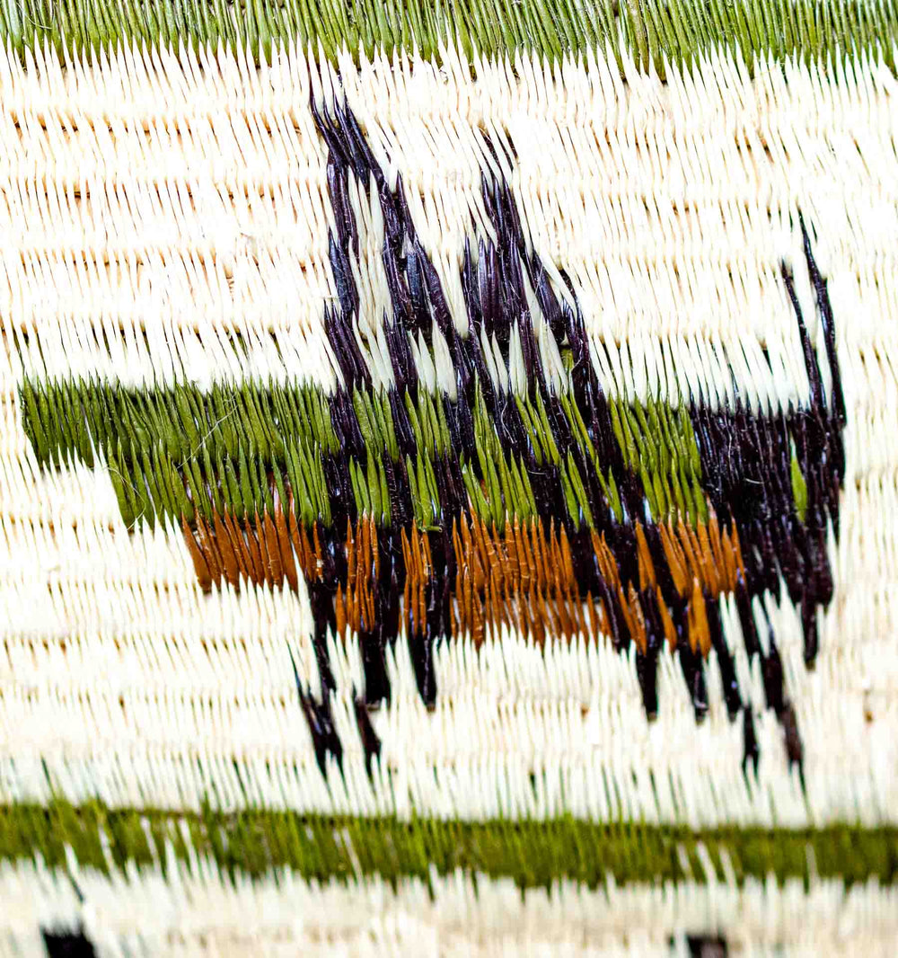 Detailed view of grasshopper motif in green, brown, and black on palm fiber.