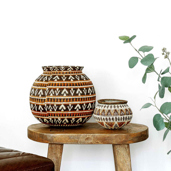 Full front view of handwoven Wounaan basket in ember tones on a wooden surface.
