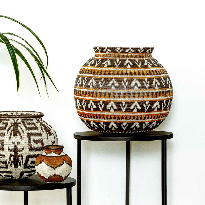 Full front view of handwoven Wounaan basket in ember tones on a wooden surface.