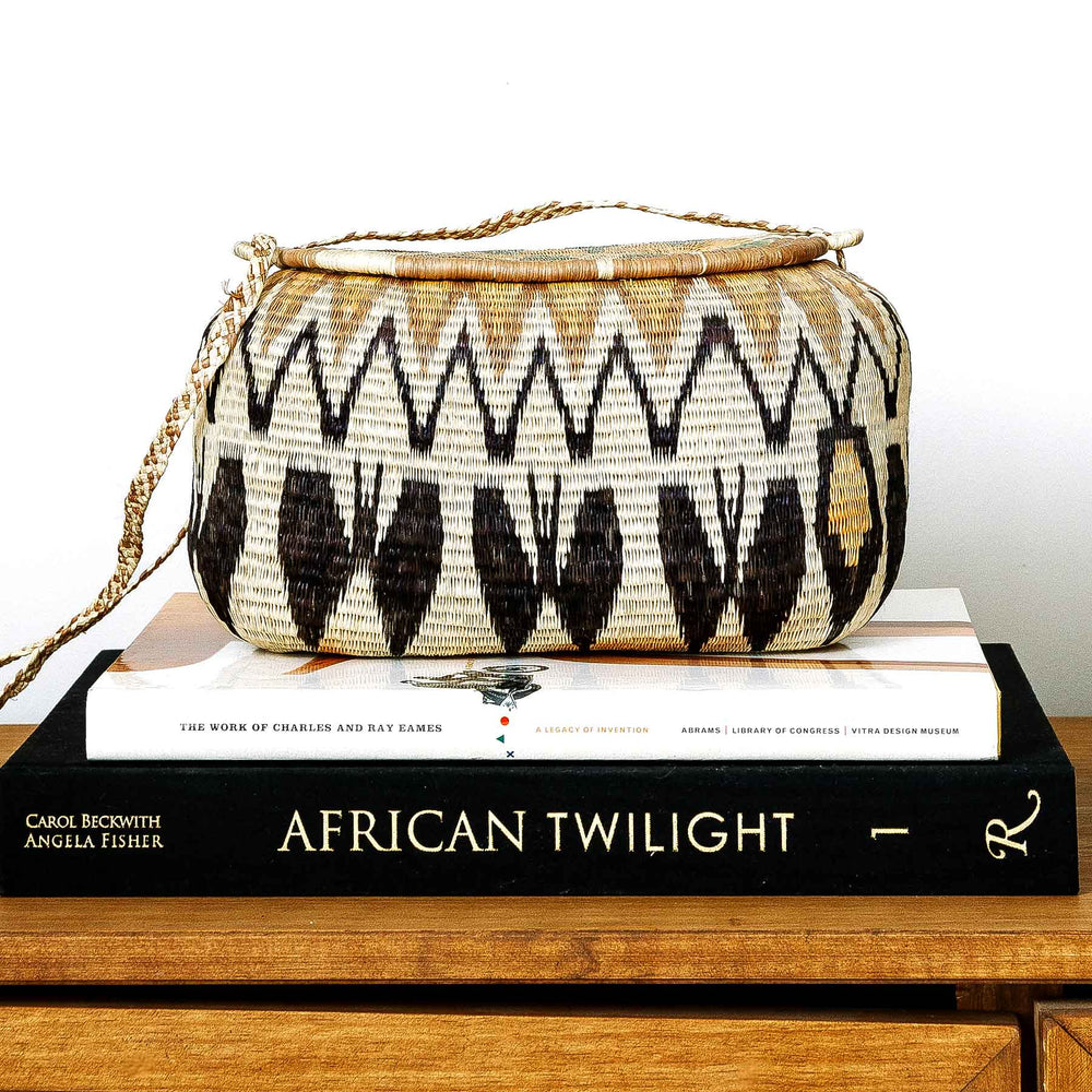 Golden peaks Wounaan basket purse displayed on stacked art books