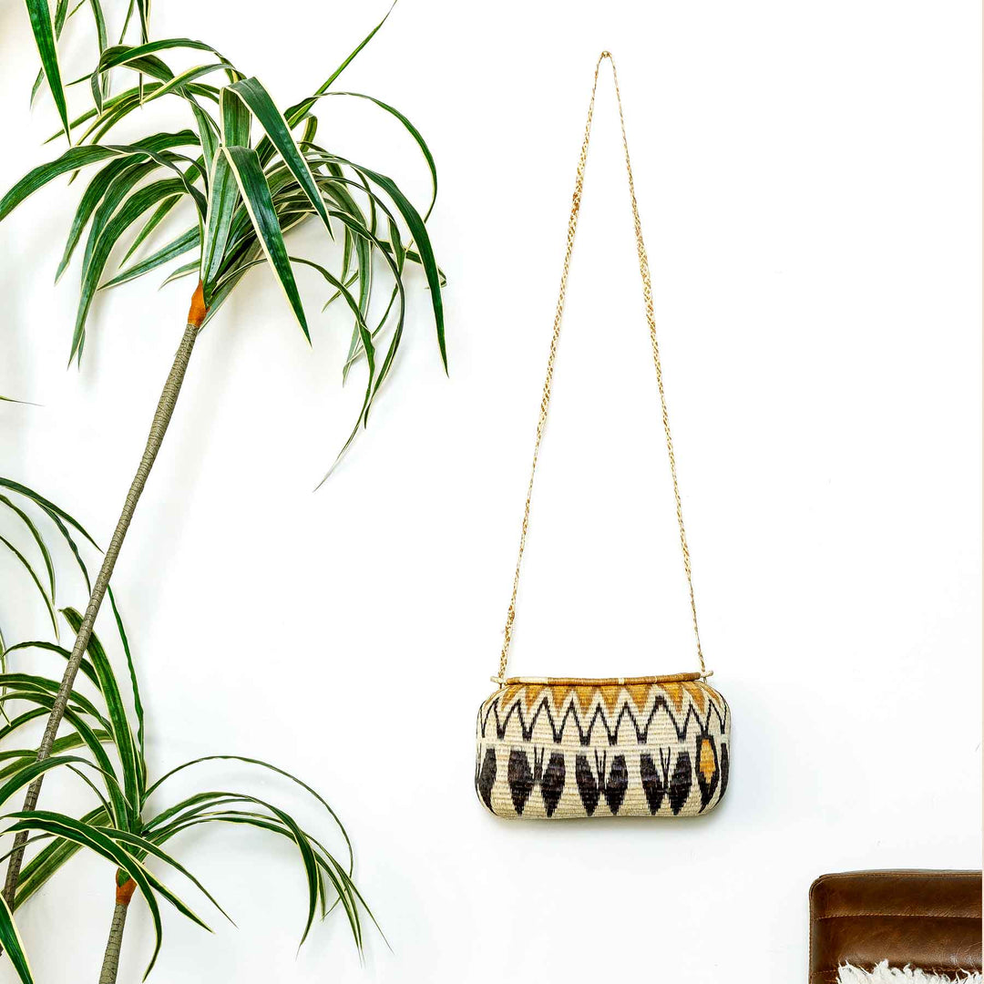 Wounaan basket purse with long braided strap hanging against white wall