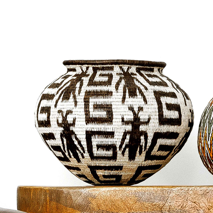 Wounaan basket with insect and geometric designs in dark brown on natural palm background.