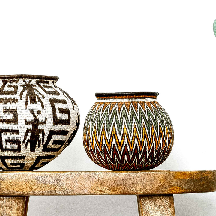 Rainforest Chevron Wounaan Basket styled beside black-and-white basket on wooden bench.