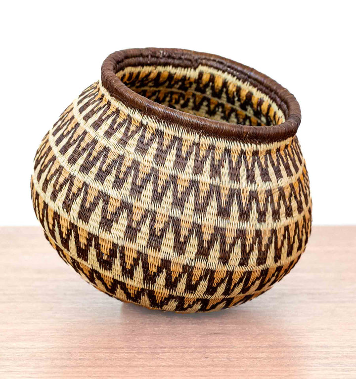 Panamanian Wounaan basket with sunburst wave pattern in brown, tan, and ivory, handwoven from dyed palm fibers.