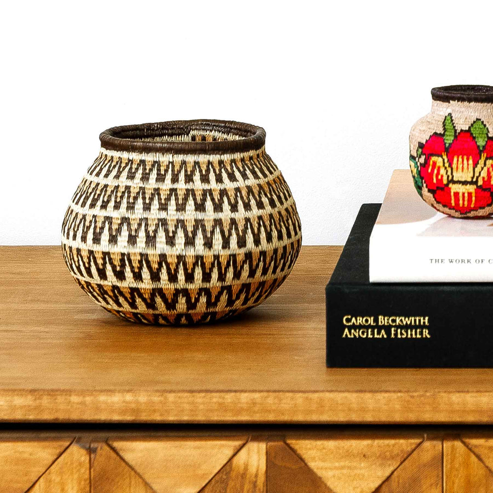 Sunburst Wave Wounaan basket displayed on console table, handwoven in Panama from palm fibers with geometric design.