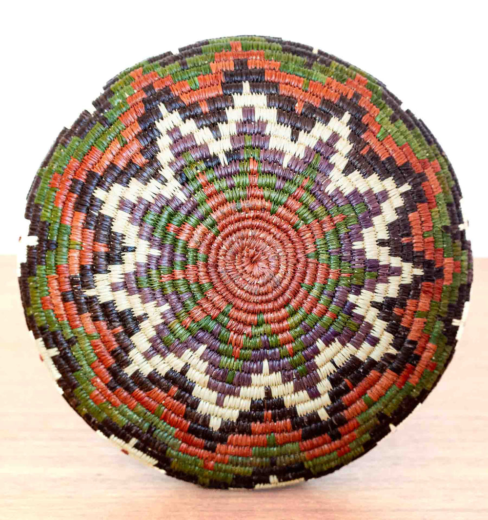 Overhead view of colorful Wounaan basket showing intricate chevron starburst pattern in palm fiber.