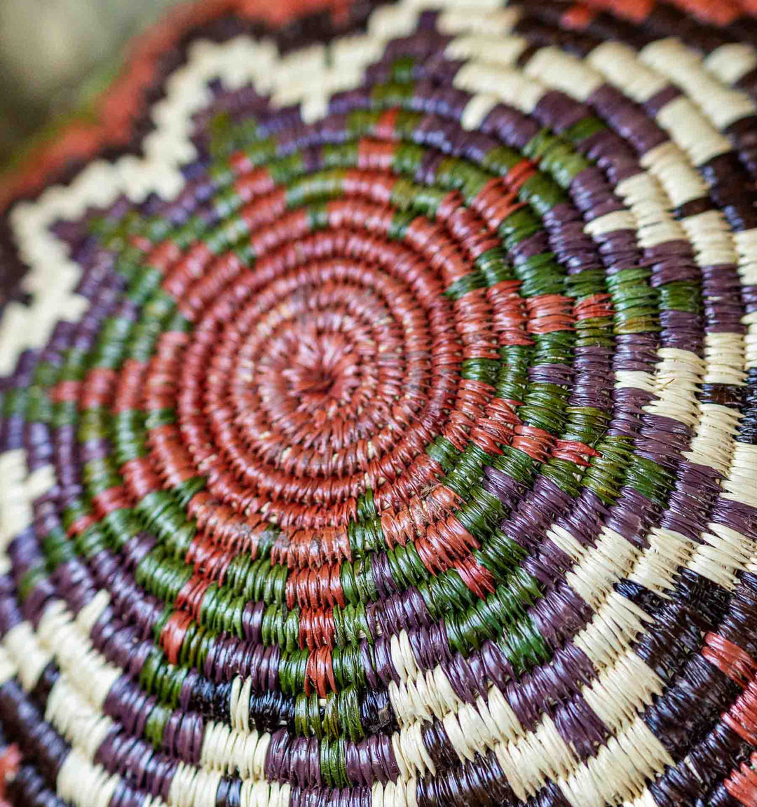 Detailed view of Wounaan woven basket base showing concentric chevron pattern in green, red, purple, ivory, and black.
