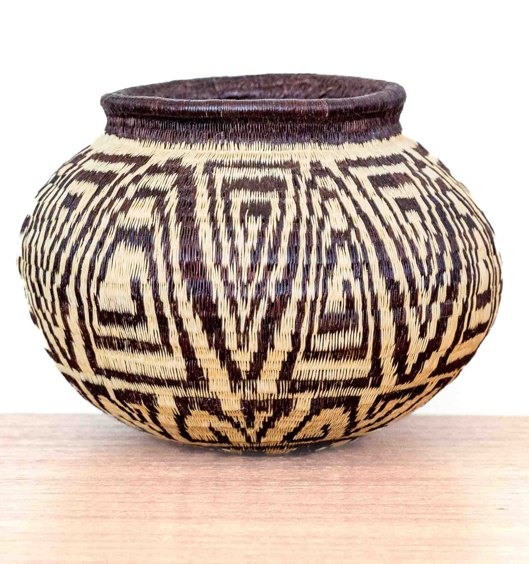 Handwoven Wounaan basket with rounded form and repeating labyrinth pattern, crafted in Panama from dyed palm fibers